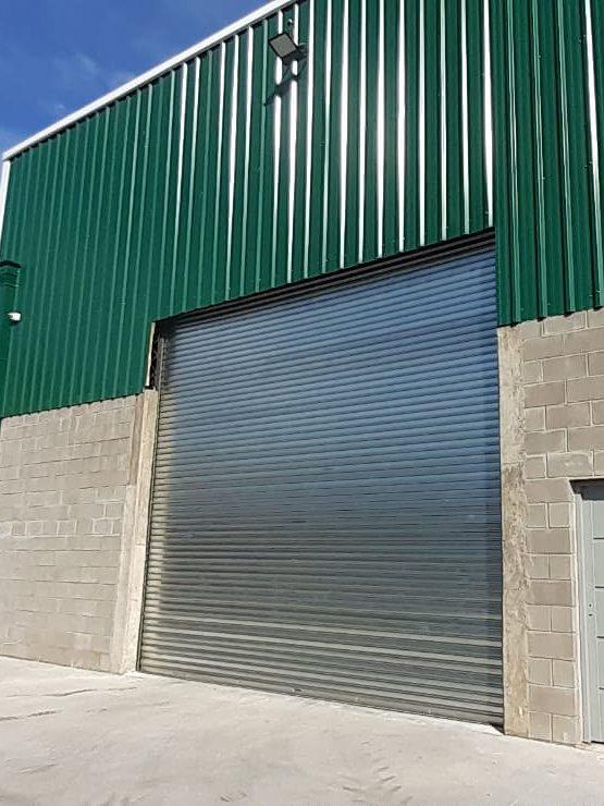 Cortina metálica gris instalada en un galpón de chapa verde