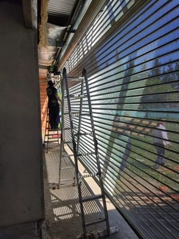Cortina metálica de lamas galvanizadas instalada en un frente, con escalera apoyada