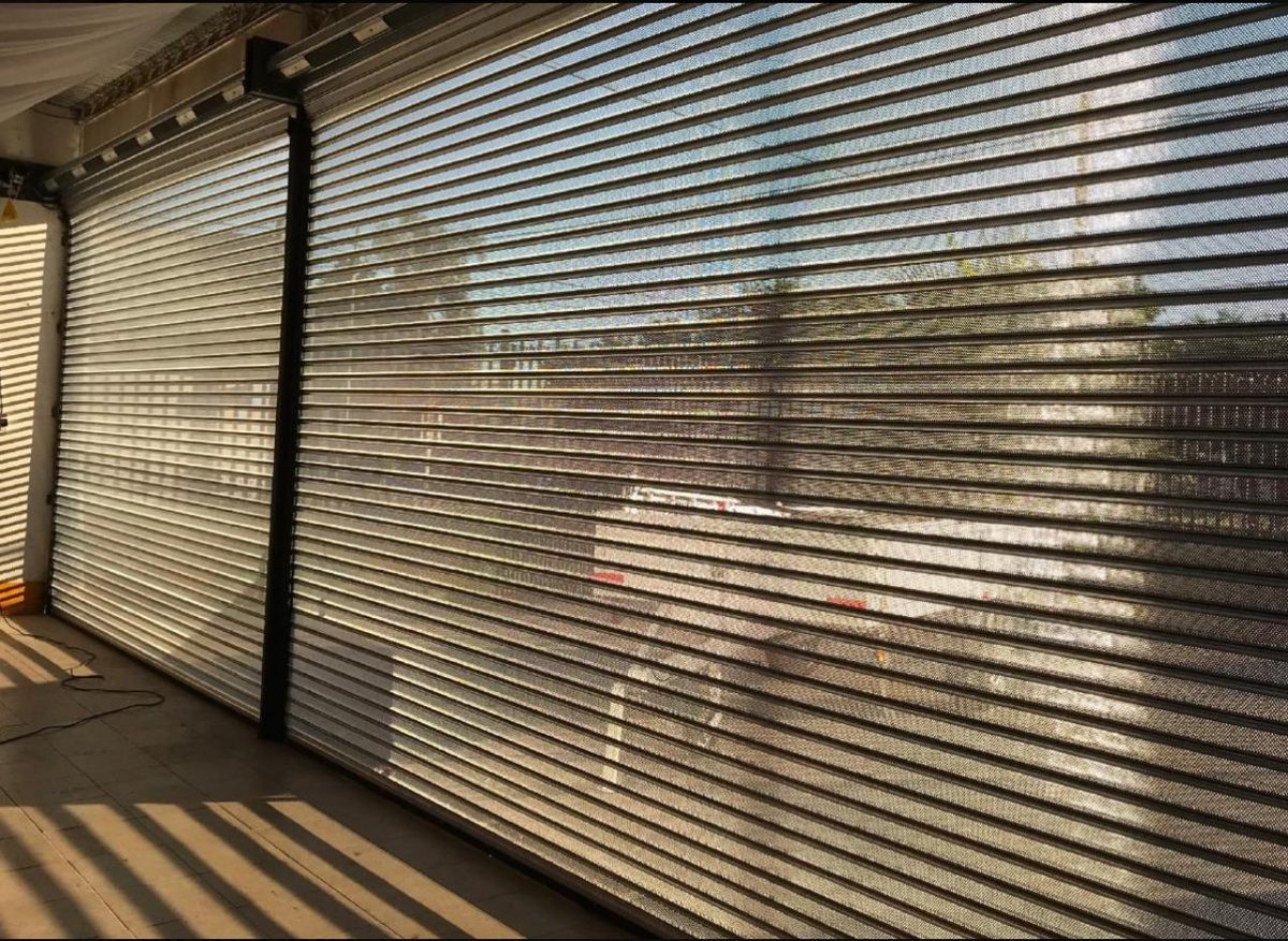 Cortinas metálicas microperforadas instaladas en un local, con el sol atravesando las lamas
