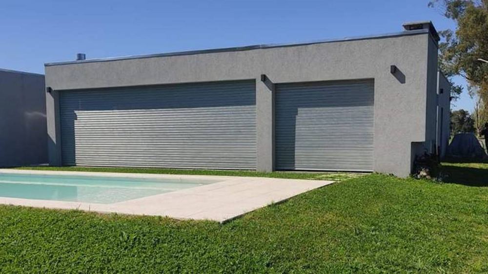 Casa con portón de garaje de dos hojas con cortinas metálicas junto a una pileta